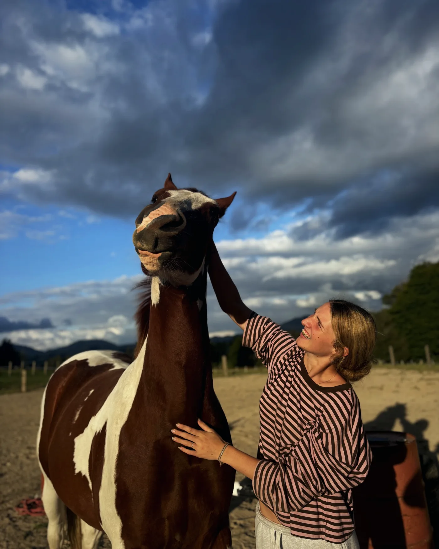 Jess Haskins smiling up at a paint horse under a dramatic sky